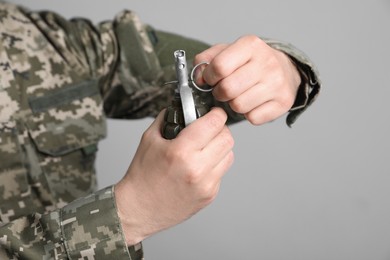 Photo of Soldier pulling safety pin out of hand grenade on light grey background, closeup. Military service