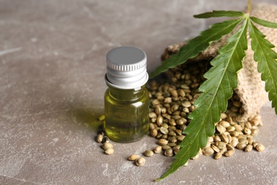 Bottle with hemp oil, seeds and leaf on gray table