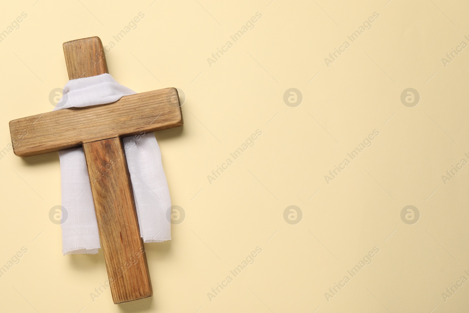 Photo of Wooden cross and white cloth on beige background, top view with space for text. Easter attributes