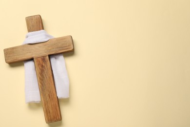 Photo of Wooden cross and white cloth on beige background, top view with space for text. Easter attributes