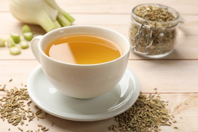 Photo of Fennel tea in cup, seeds and fresh vegetable on light wooden table, closeup