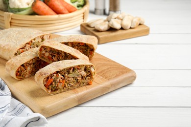 Photo of Cut tasty strudel with chicken and vegetables on white wooden table. Space for text