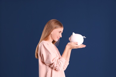 Teen girl with piggy bank on color background