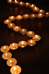 Burning candles on wooden table in darkness