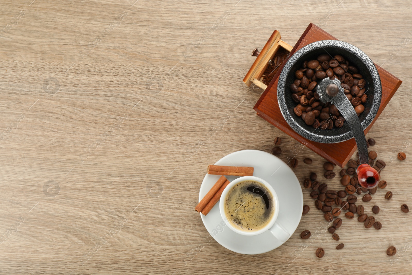 Photo of Vintage manual coffee grinder with beans, cinnamon and cup of aromatic drink on wooden table, flat lay. Space for text