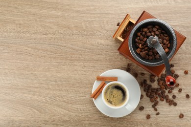 Vintage manual coffee grinder with beans, cinnamon and cup of aromatic drink on wooden table, flat lay. Space for text