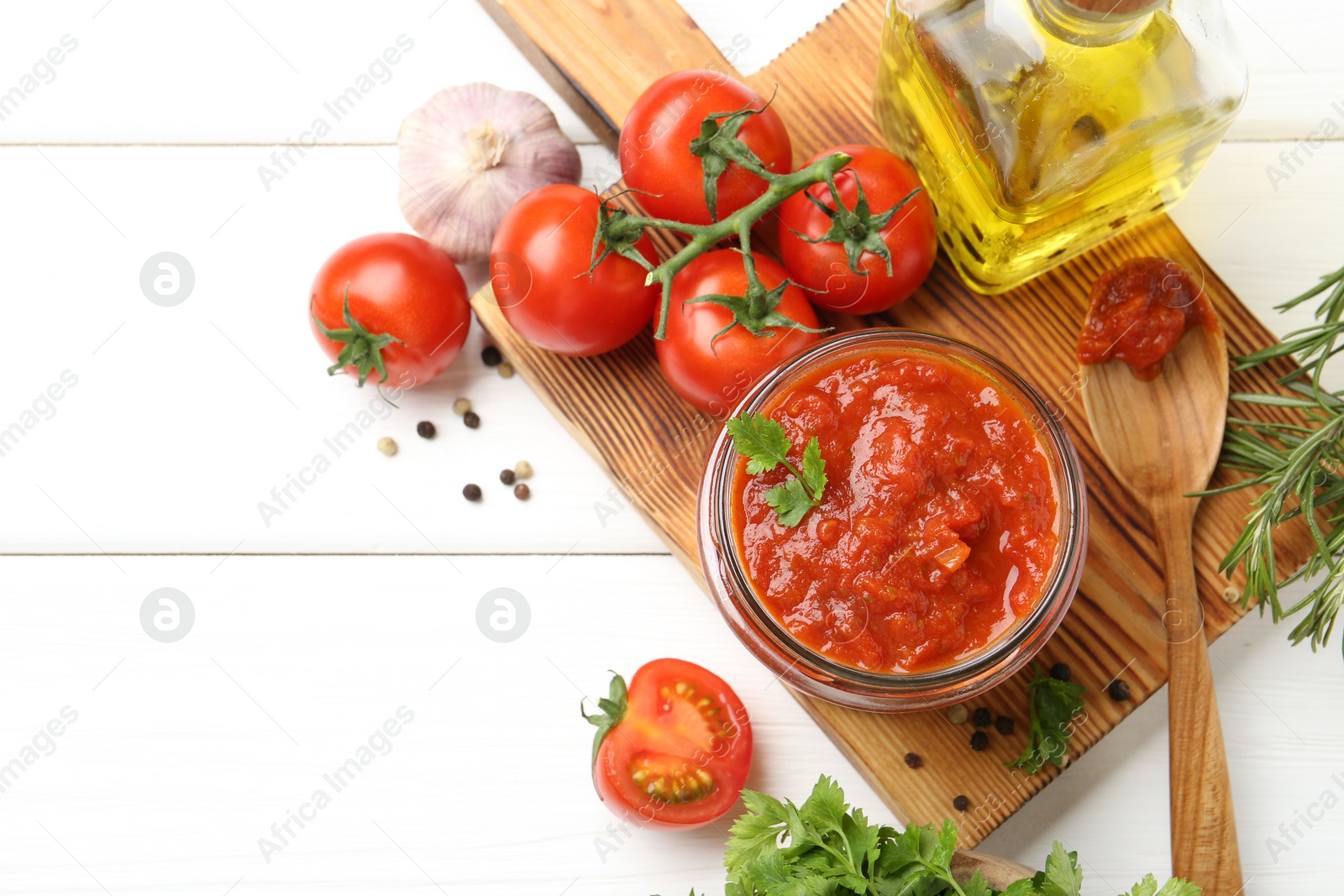 Photo of Homemade tomato sauce in jar, spoon and fresh ingredients on white wooden table, flat lay. Space for text