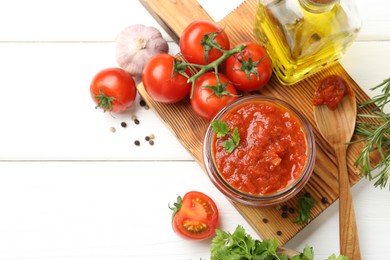 Homemade tomato sauce in jar, spoon and fresh ingredients on white wooden table, flat lay. Space for text