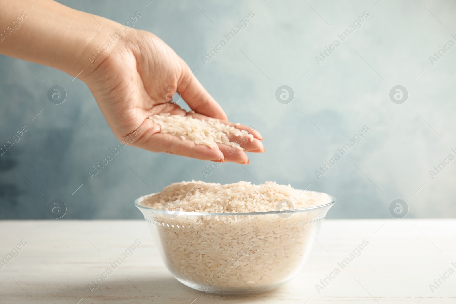 Photo of Woman holding uncooked rice over bowl at table, closeup