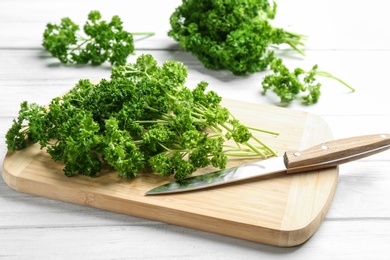 Photo of Fresh curly parsley, cutting board and knife on white wooden table