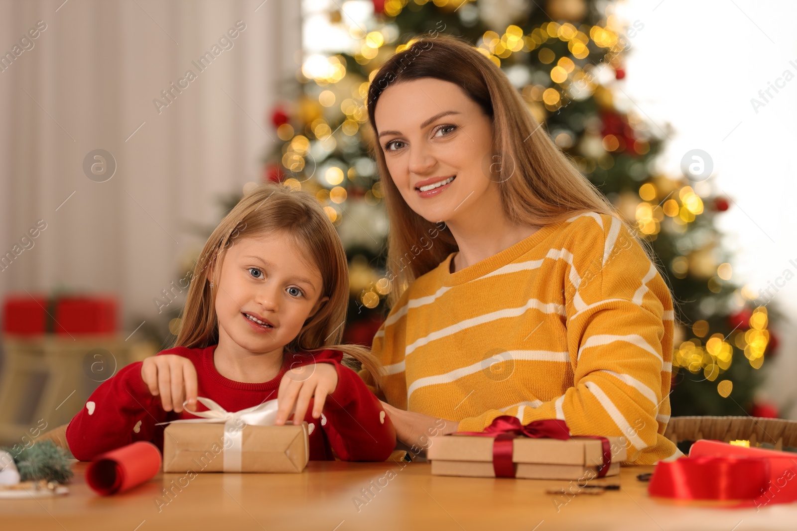 Photo of Christmas presents wrapping. Mother and her little daughter tying ribbon bows on gift boxes at home