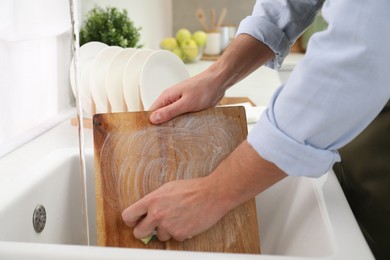 Photo of Man washing wooden cutting board in kitchen sink, closeup