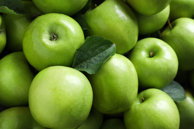 Pile of tasty green apples with leaves as background, closeup