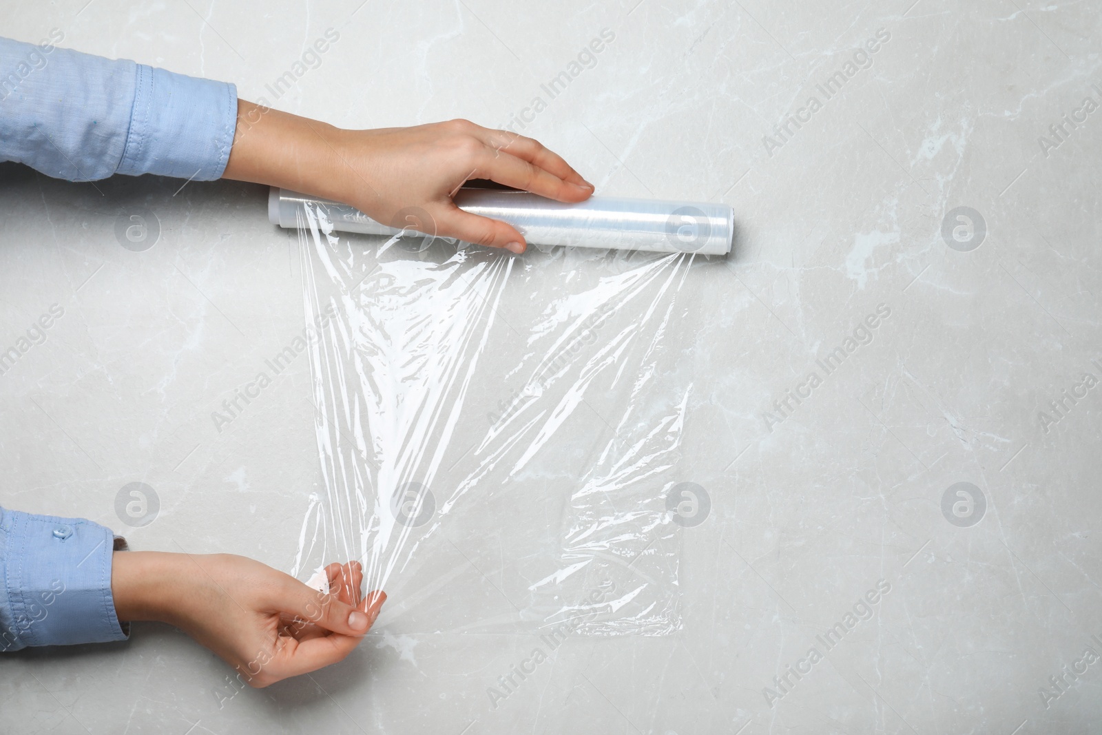 Photo of Woman with roll of stretch wrap at light grey table, top view