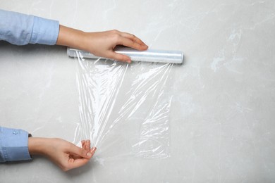 Photo of Woman with roll of stretch wrap at light grey table, top view