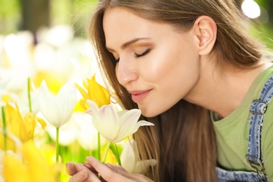 Beautiful young woman near blossoming tulips in green park on sunny spring day