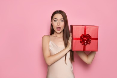 Portrait of emotional young woman with gift box on pink background