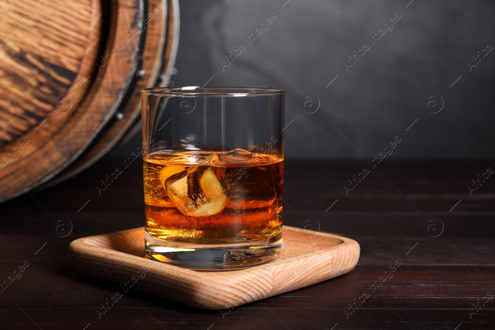 Photo of Glass of whiskey with ice cubes and wooden barrel on table