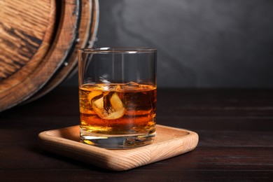 Glass of whiskey with ice cubes and wooden barrel on table