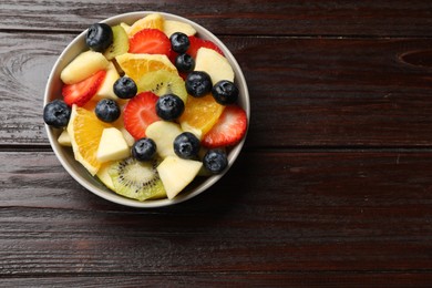 Photo of Tasty fruit salad in bowl on wooden table, top view. Space for text