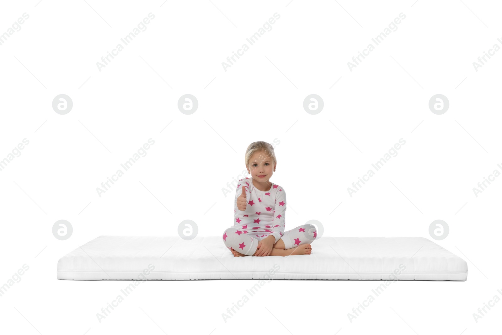 Photo of Little girl sitting on mattress and showing thumb up against white background