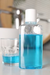 Photo of Bottle and glass of mouthwash on white countertop in bathroom