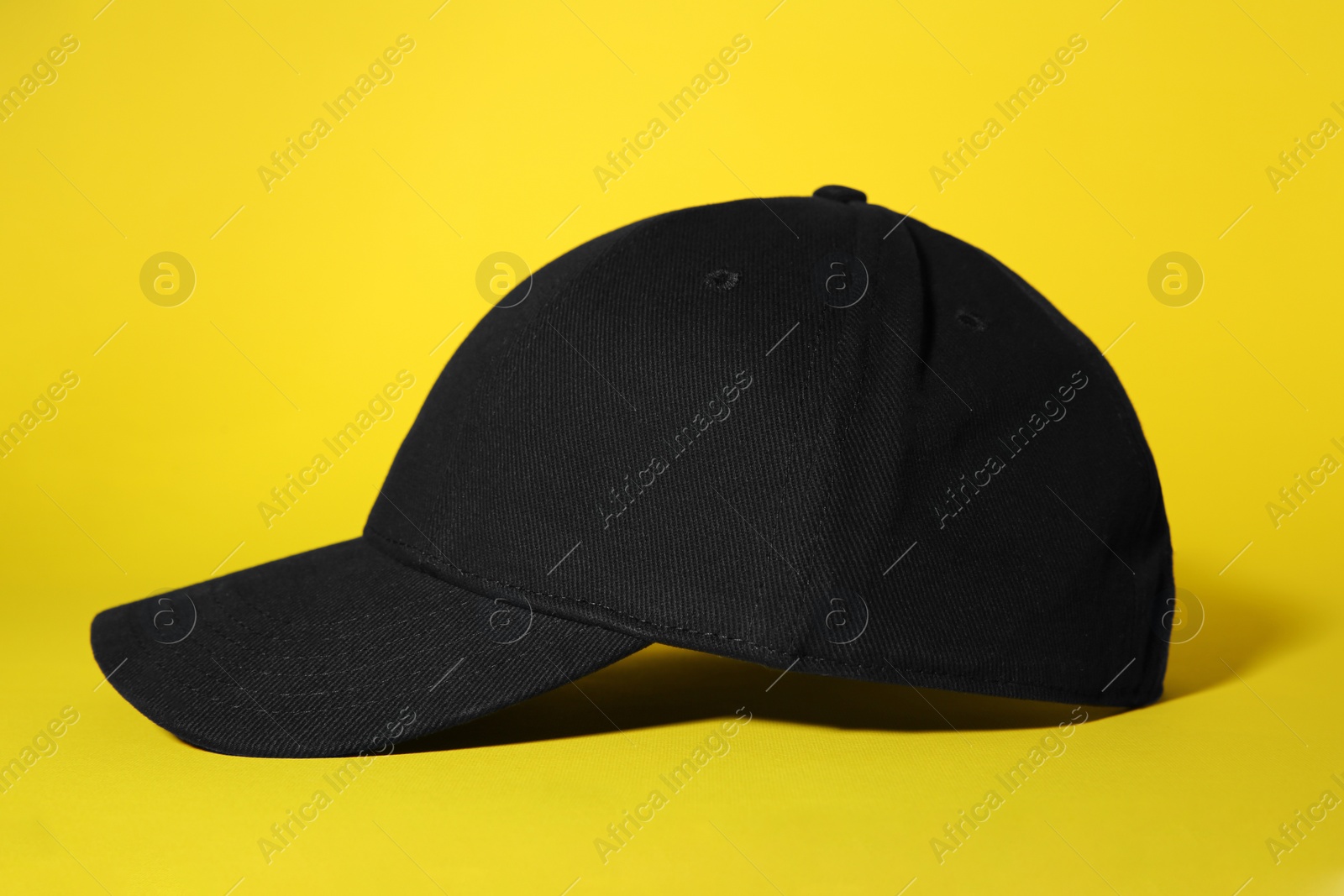 Photo of Stylish black baseball cap on yellow background