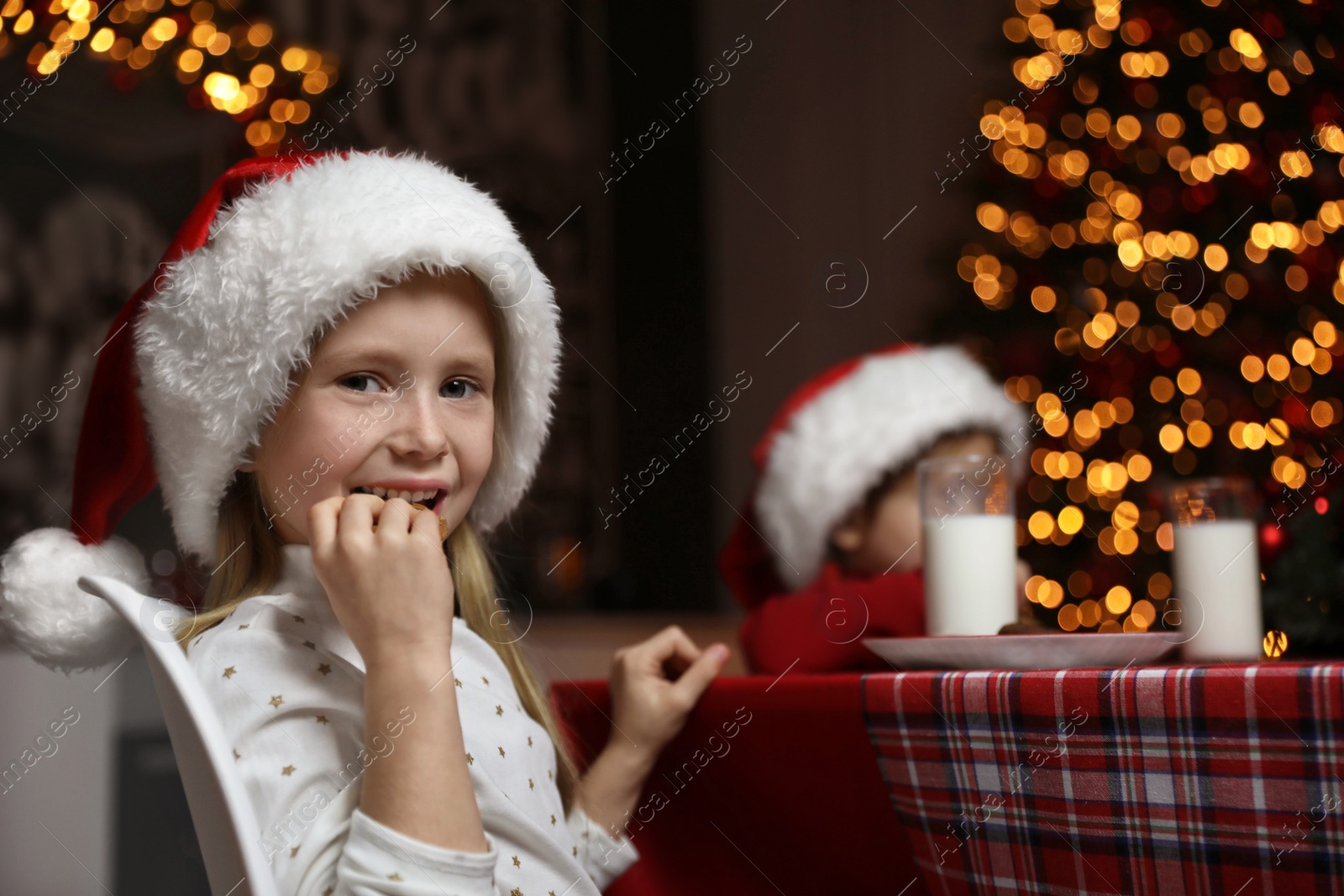 Photo of Cute little children eating cookies at table in dining room. Christmas time