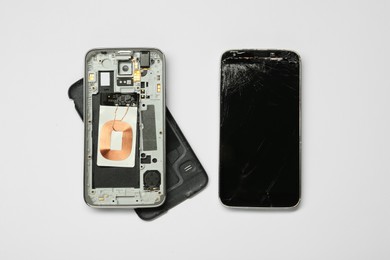 Photo of Damaged smartphone on white background, flat lay. Device repairing
