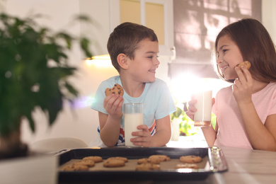 Photo of Cute little children eating cookies with milk in kitchen. Cooking pastry