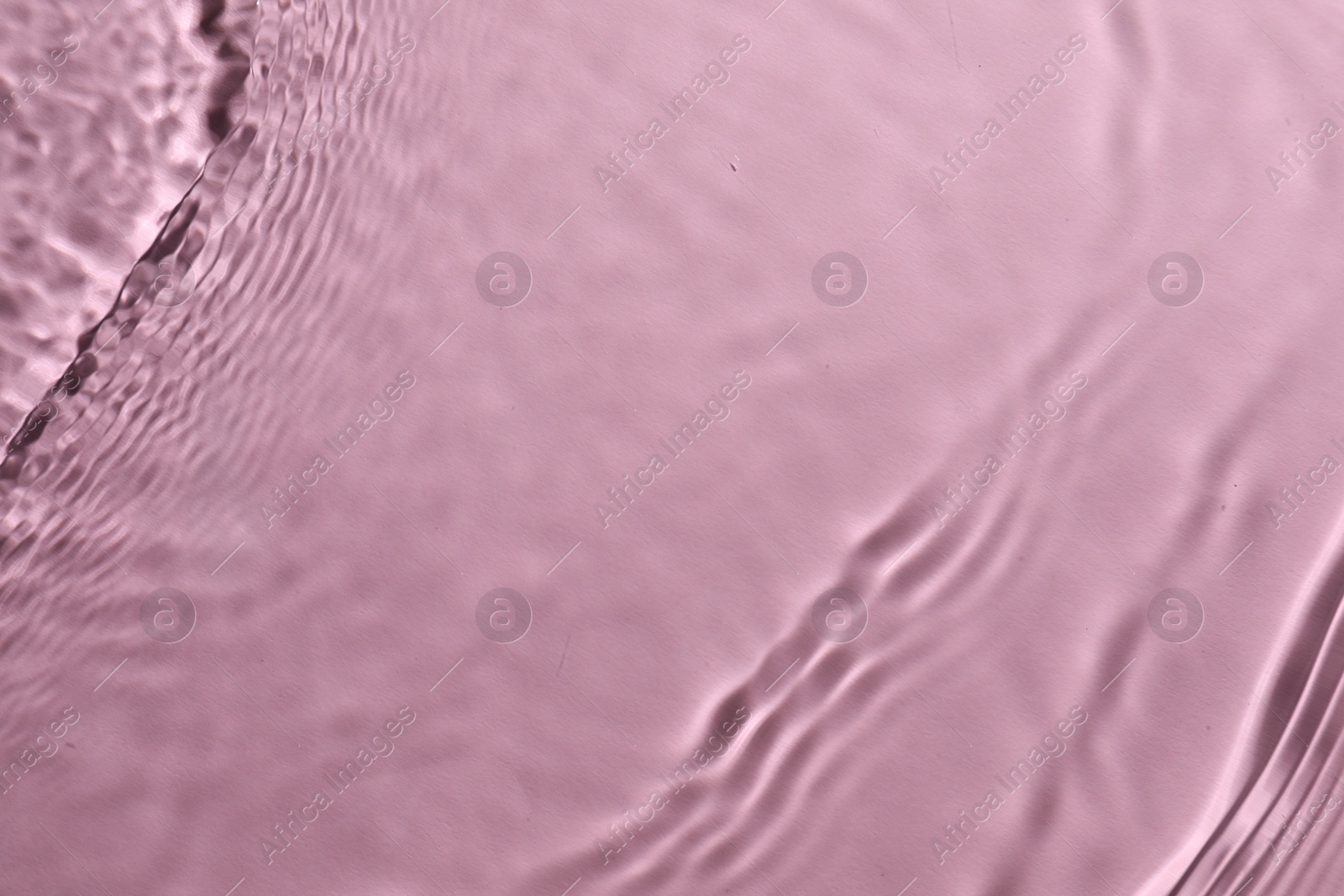 Photo of Rippled surface of clear water on pink background, top view