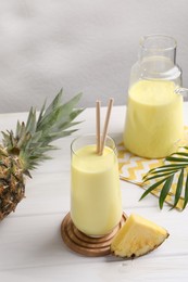 Tasty pineapple smoothie and fruit on white wooden table