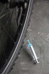Photo of Bike wheel with syringe on grey background, closeup. Using doping in cycling sport concept