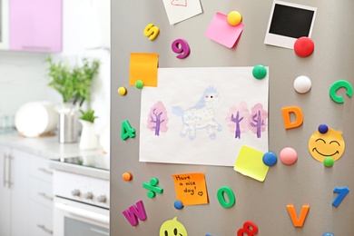 Sheets of paper, child's drawing and magnets on refrigerator door in kitchen. Space for text