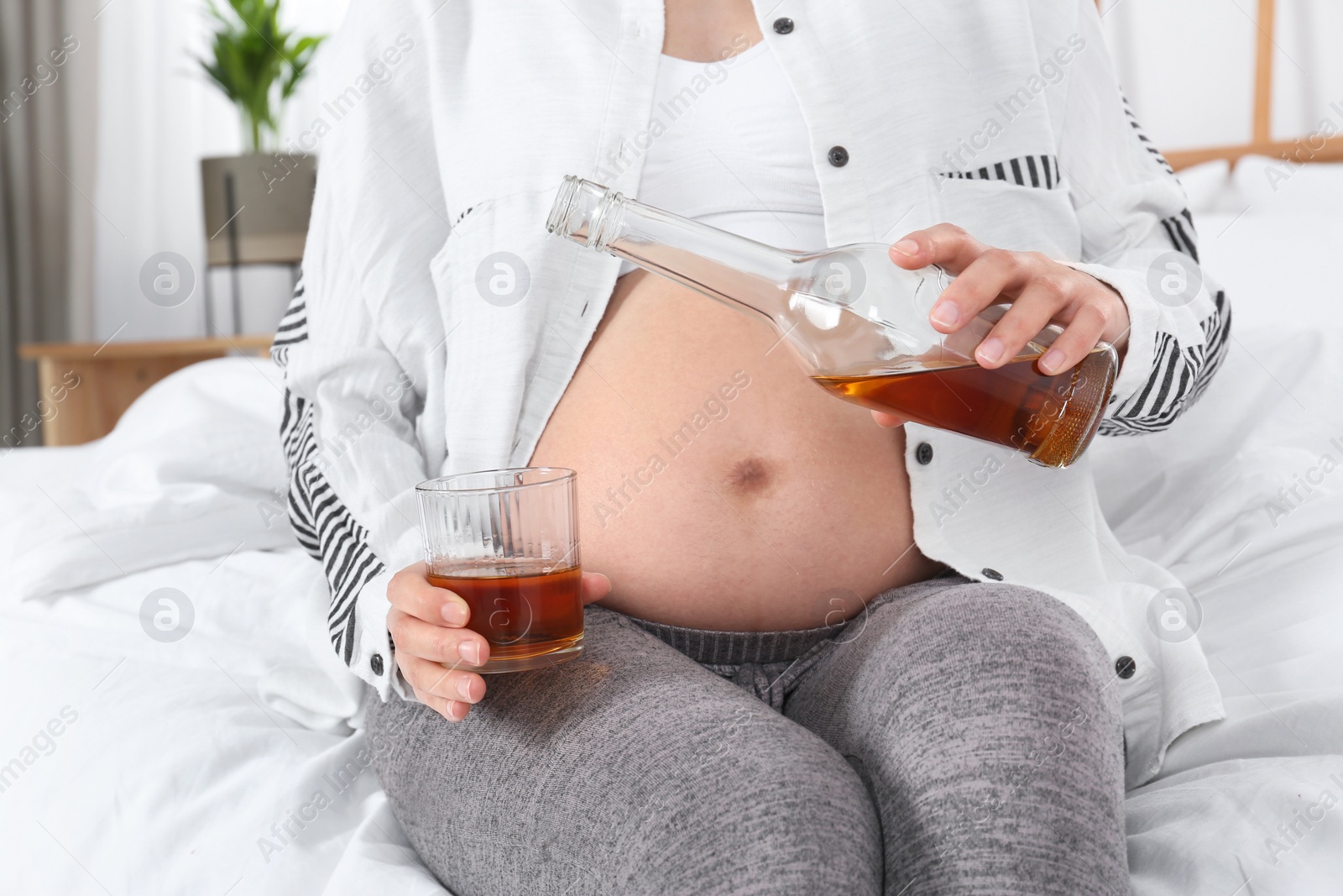 Photo of Pregnant woman pouring whiskey into glass at home. Alcohol addiction