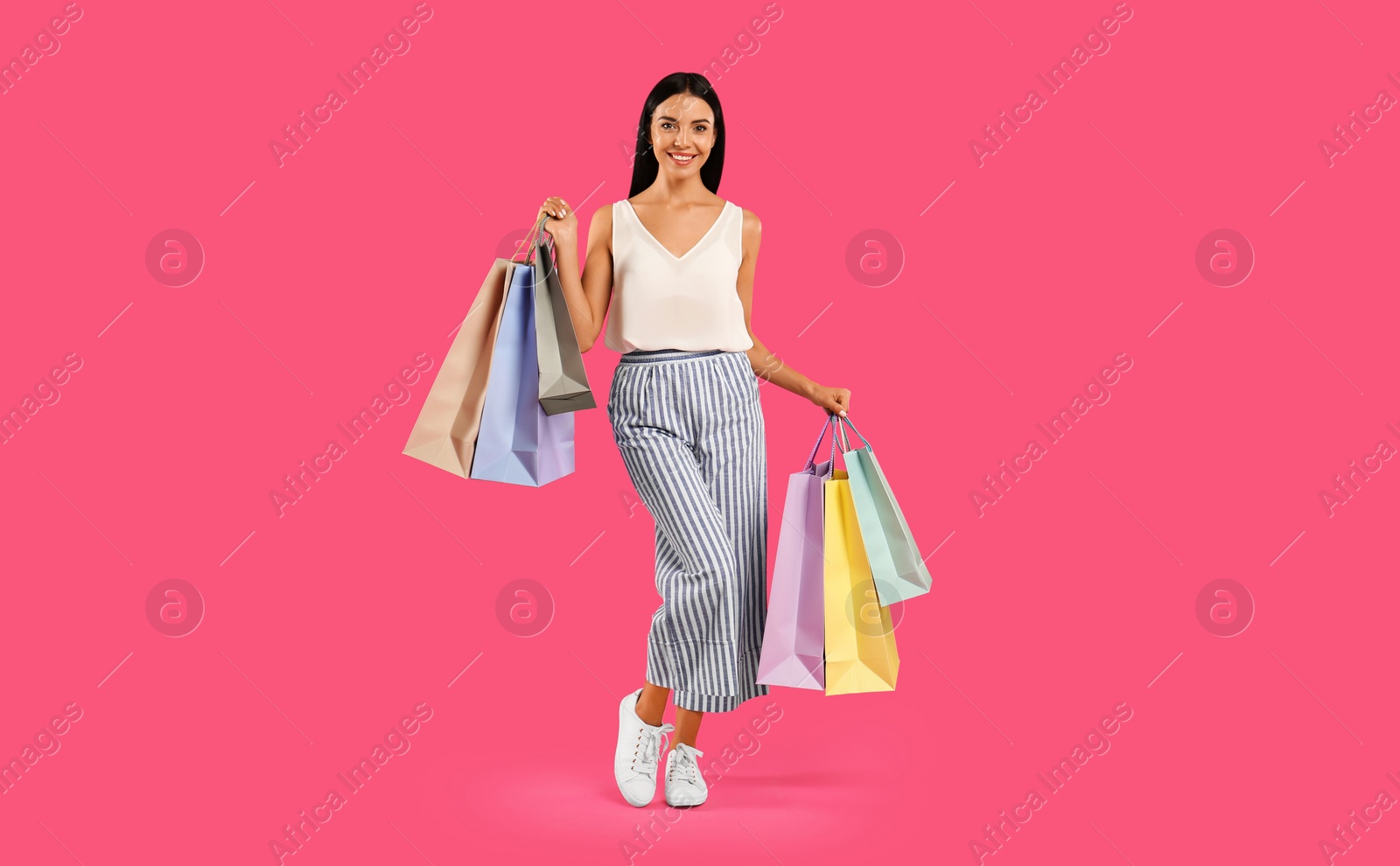 Photo of Beautiful young woman with paper shopping bags on pink background