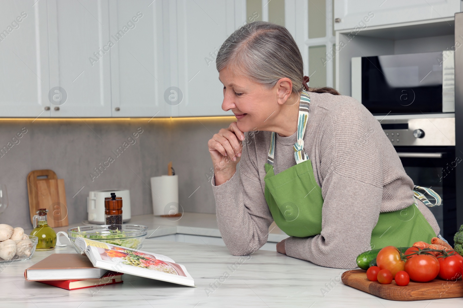 Photo of Happy woman with recipe book at table in kitchen