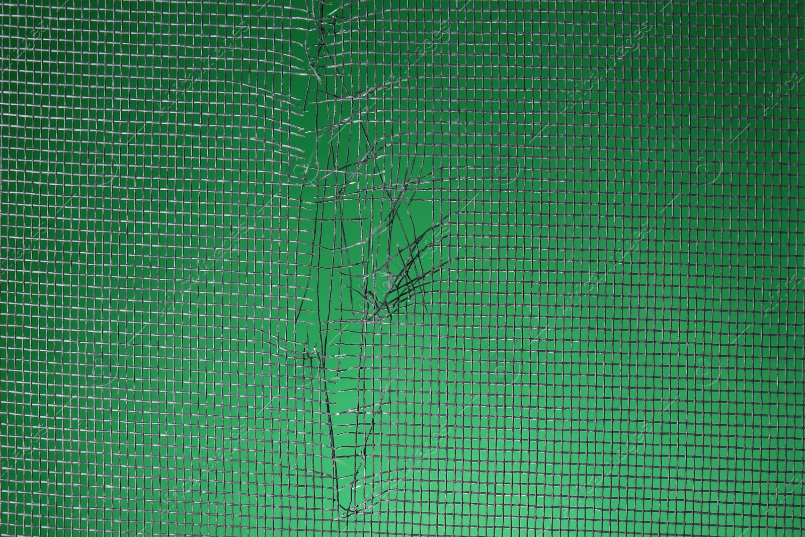 Photo of Torn window screen against green background, closeup