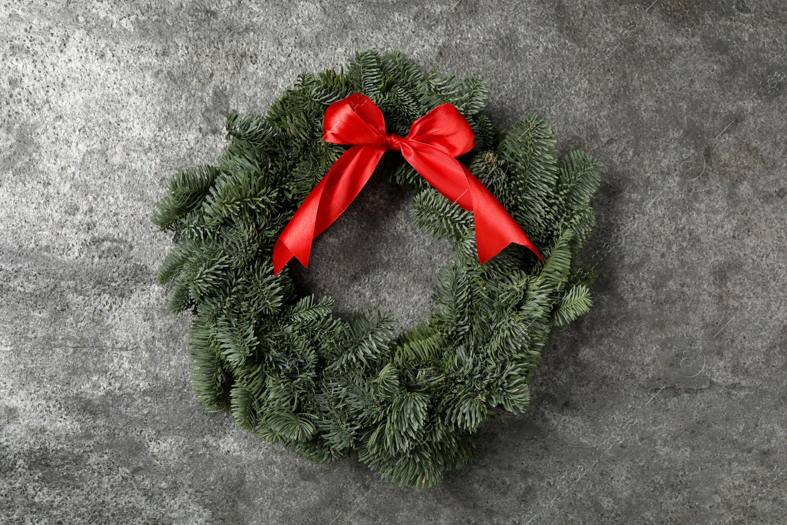 Photo of Christmas wreath made of fir tree branches with red ribbon on grey background