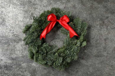 Christmas wreath made of fir tree branches with red ribbon on grey background