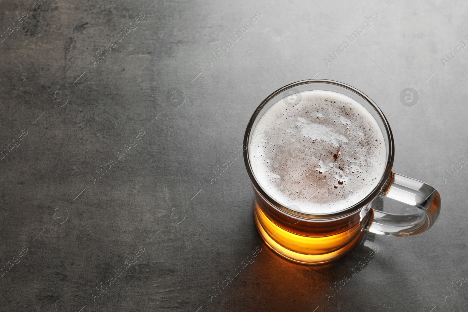 Photo of Glass mug with cold tasty beer on grunge background, view from above