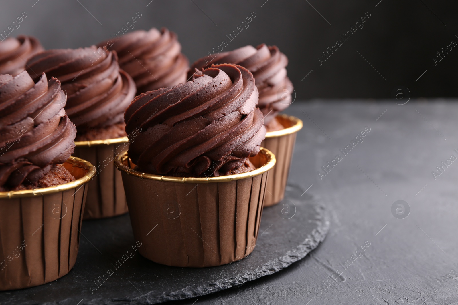 Photo of Delicious chocolate cupcakes on black textured table, closeup. Space for text