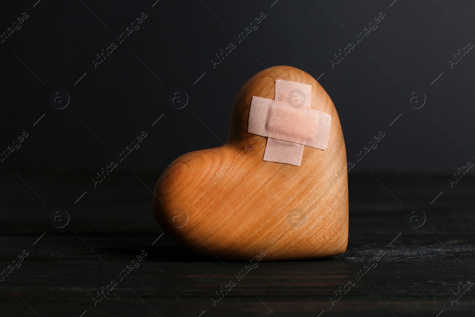 Photo of Wooden heart with adhesive plasters in darkness on table