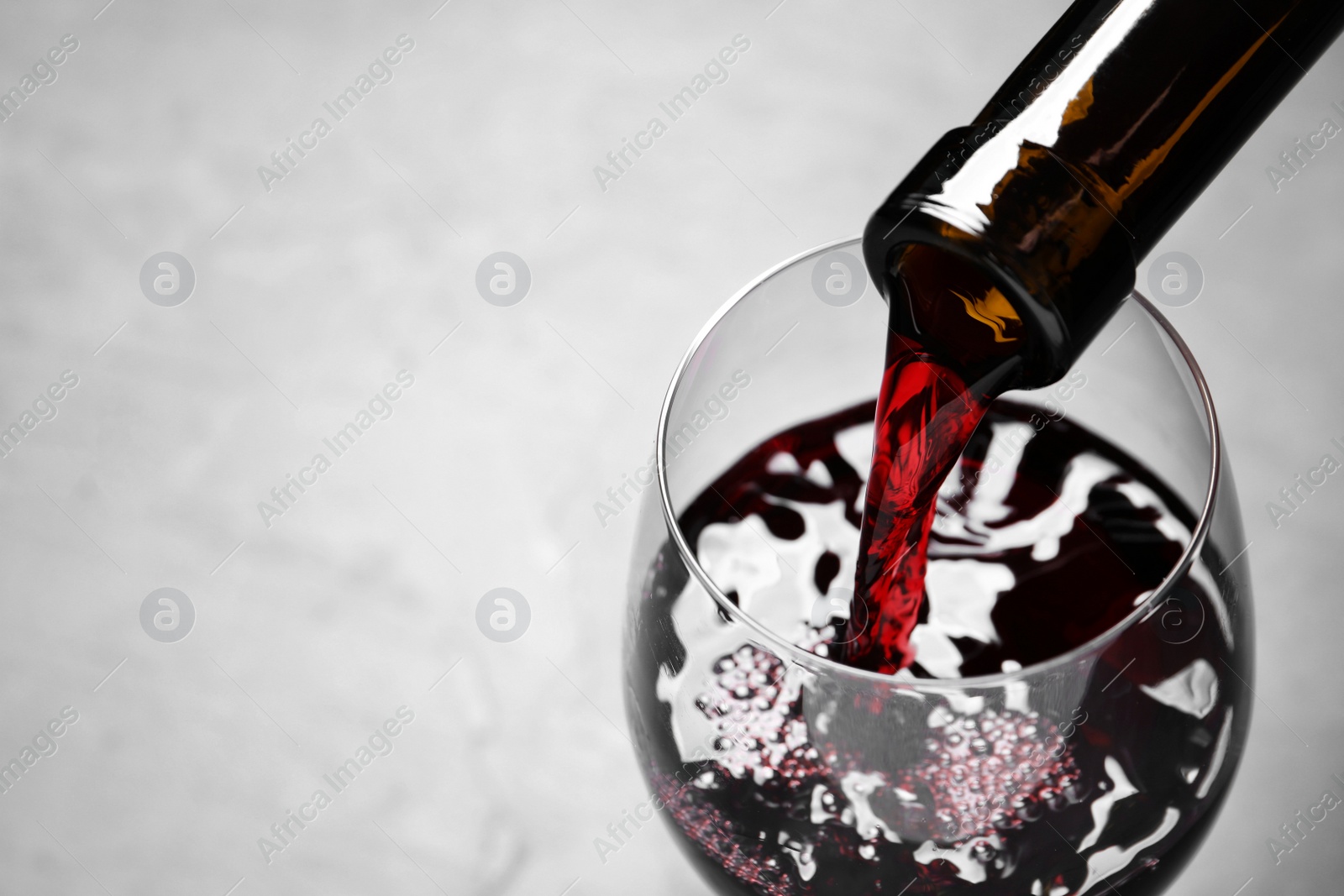 Photo of Pouring red wine from bottle into glass on light background, closeup. Space for text