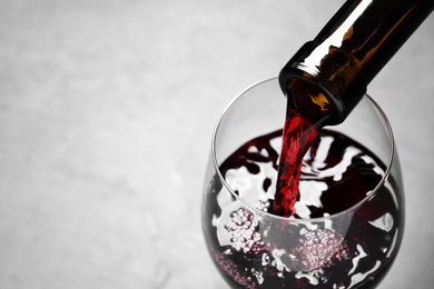 Pouring red wine from bottle into glass on light background, closeup. Space for text