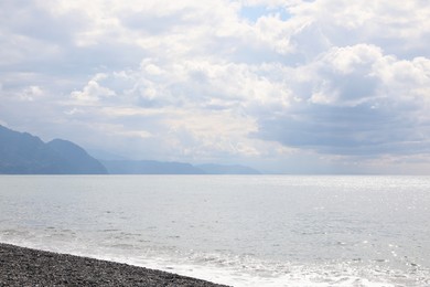 Photo of Picturesque view of beautiful sea shore and mountains under sky with fluffy clouds