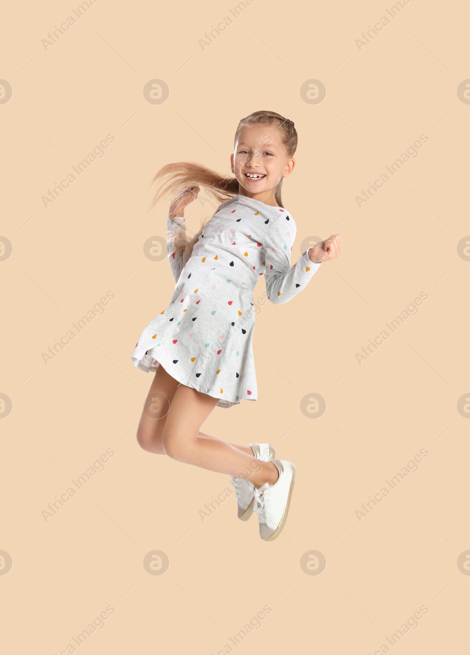 Image of Happy cute girl jumping on beige background