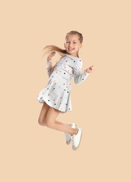 Happy cute girl jumping on beige background