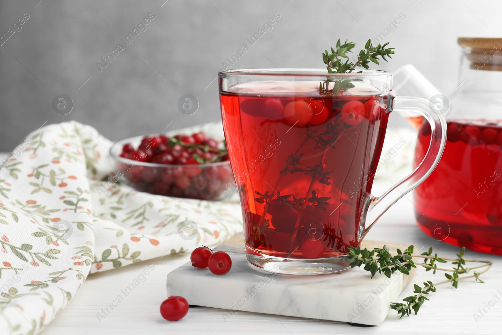 Photo of Tasty hot cranberry tea with thyme and fresh berries in glass cup on white wooden table