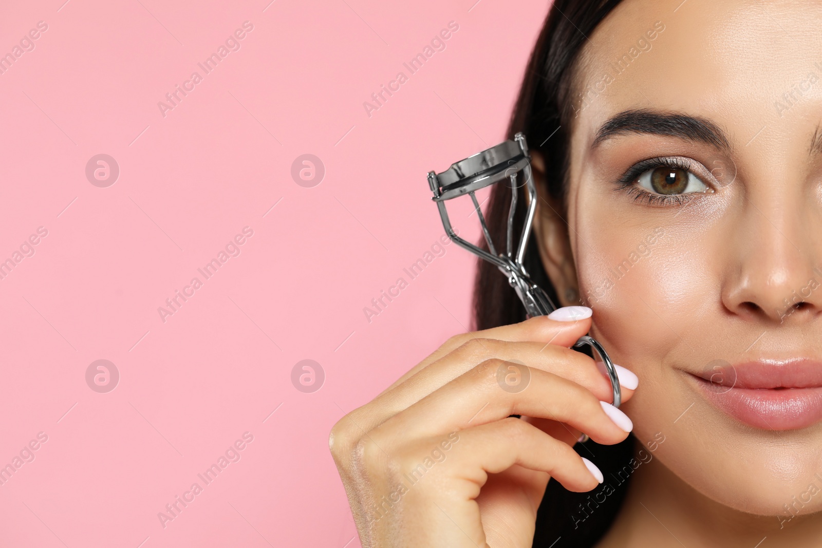 Photo of Beautiful young woman with eyelash curler on light pink background, closeup. Space for text
